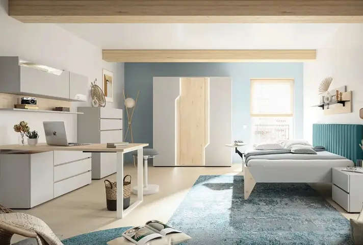 Grosser Raum mit weissem Schreibtisch und Stauraummöbeln links, in der Mitte Kleiderschrank vor blauer Wand, rechts Bett mit türkisfarbenem Kopfteil und grossem blauem Teppich.